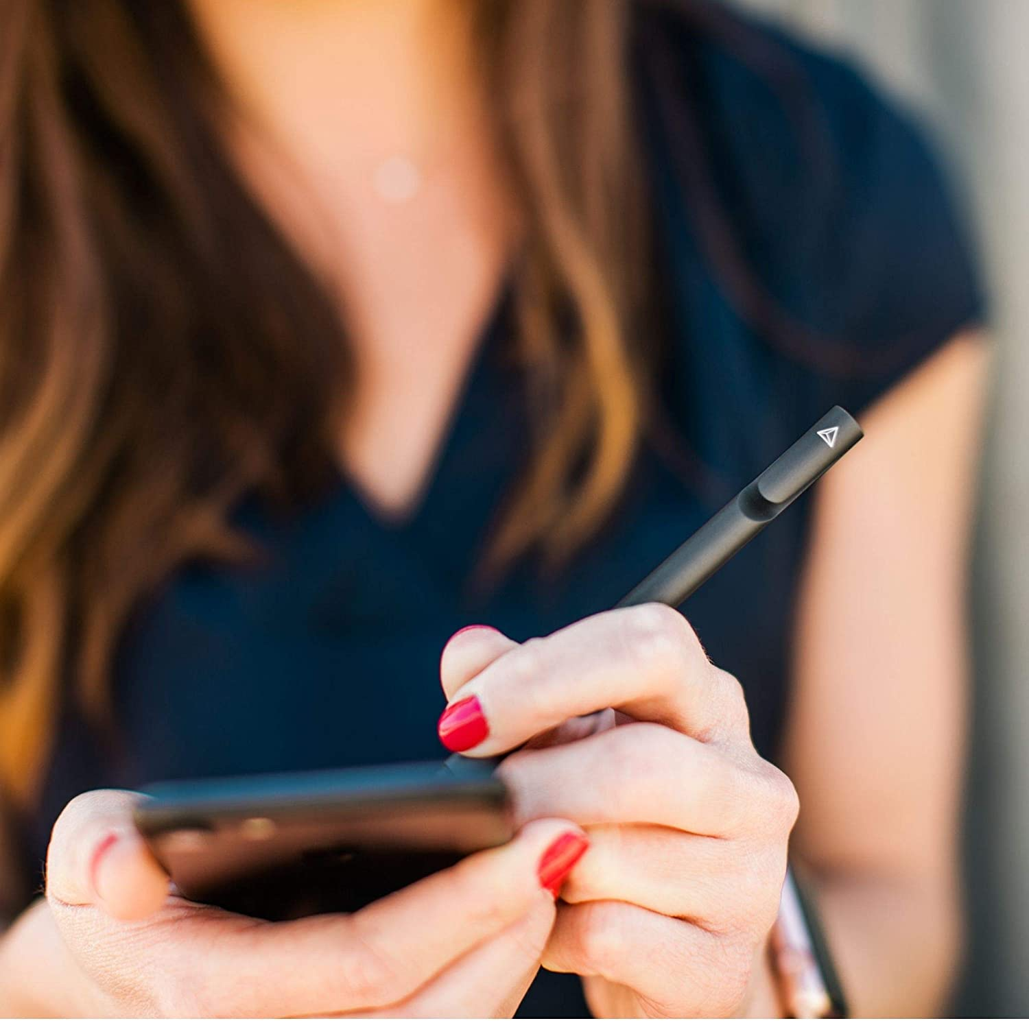 Una persona tiene in mano una penna stilo nera e la usa su uno smartphone. Smalto rosso visibile.