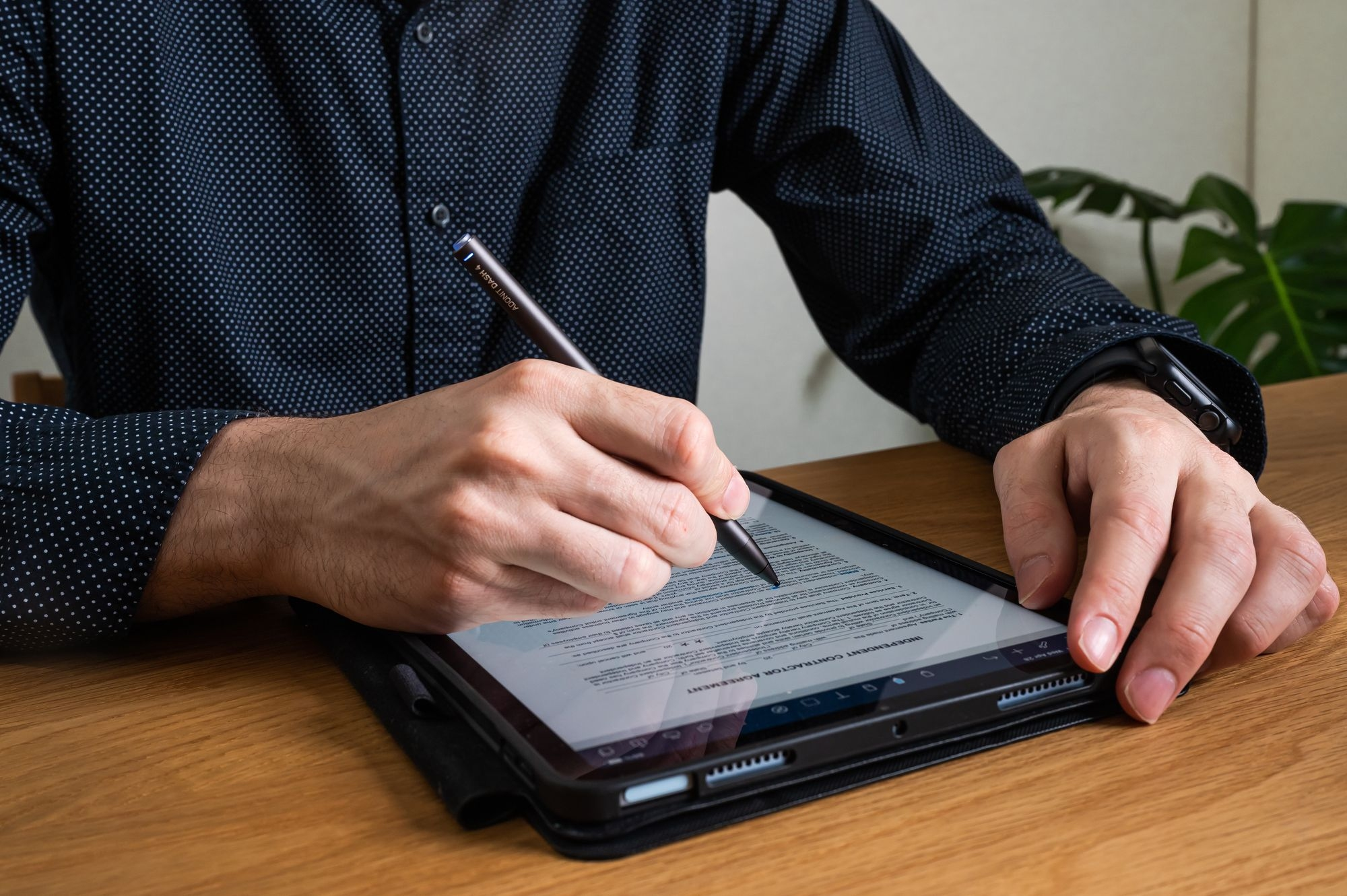 Persona che firma un documento su un tablet con una penna. Il tablet è su un tavolo di legno.