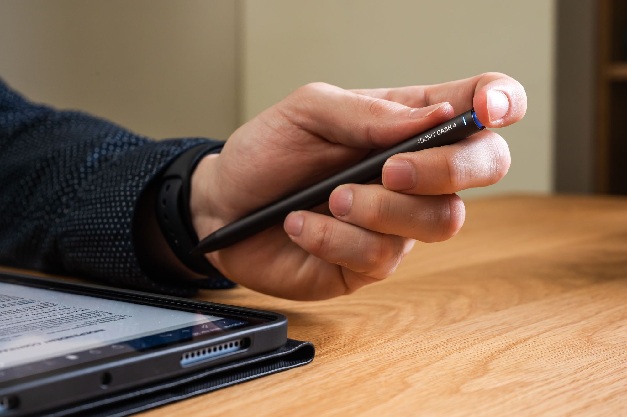 Una mano che tiene uno stilo nero vicino a un tablet su un tavolo di legno.
