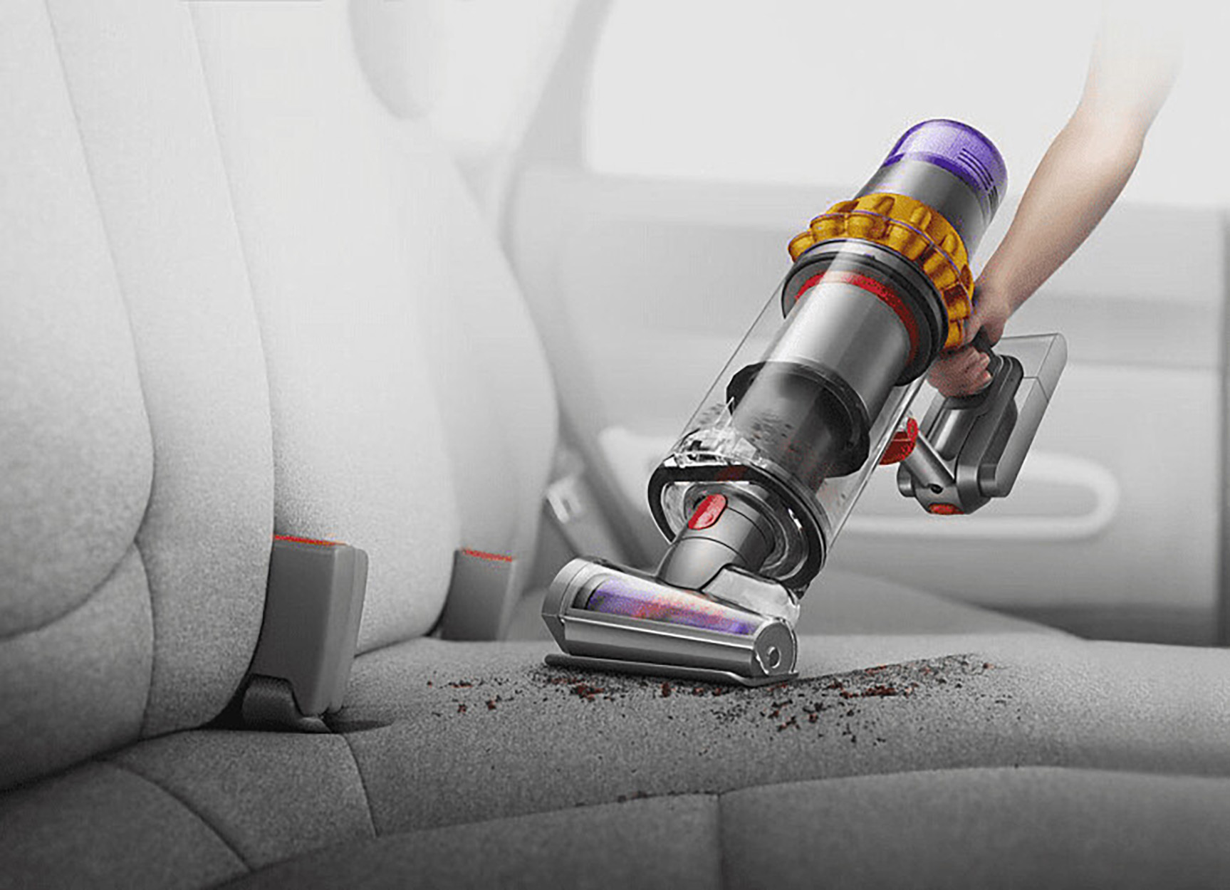 Eine Person saugt mit einem Dyson-Staubsauger einen Autositz ab.
