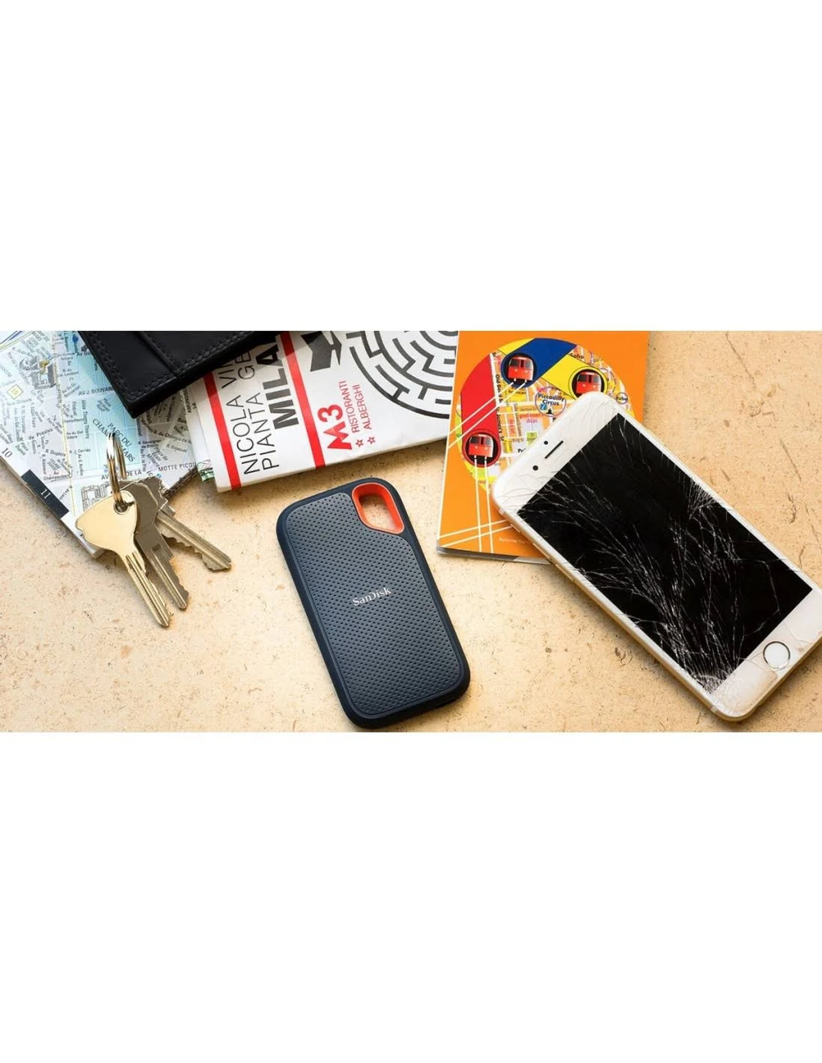 Teléfono roto, llaves, cartera y unidad SanDisk sobre superficie beige, mapa y libro.
