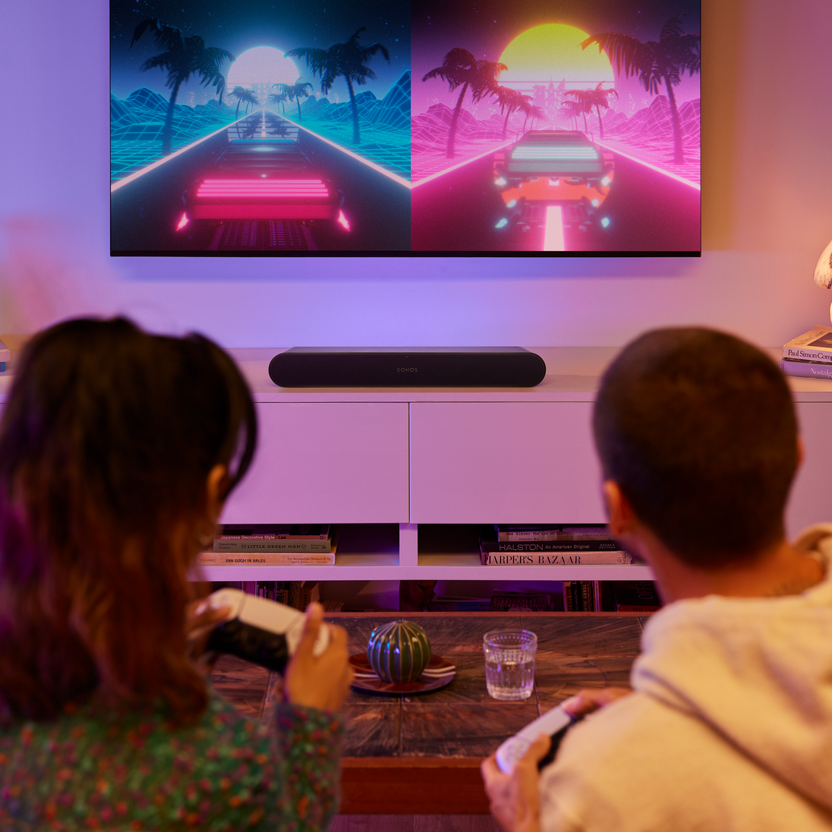 Zwei Personen spielen vor einem Fernseher mit Soundbar, der eine Videospielszenen zeigt.