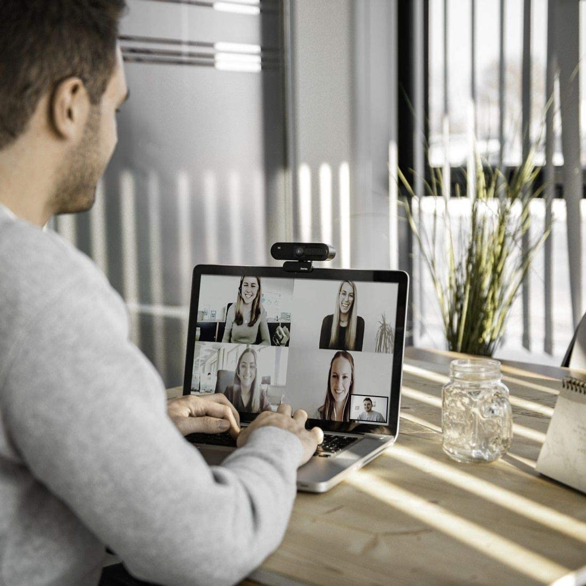 Mężczyzna używa laptopa z rozmową wideo, widzi pięć osób. Słoik, roślina.