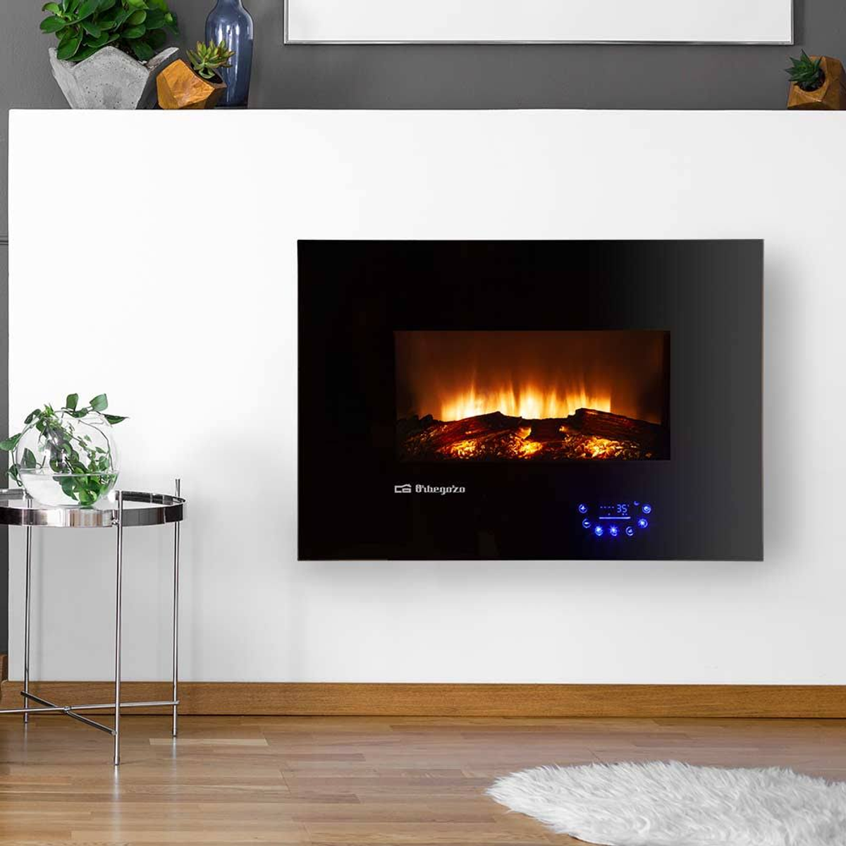 Chimenea negra en una pared blanca. Tiene un efecto de llama y está cerca de una mesa y una alfombra.