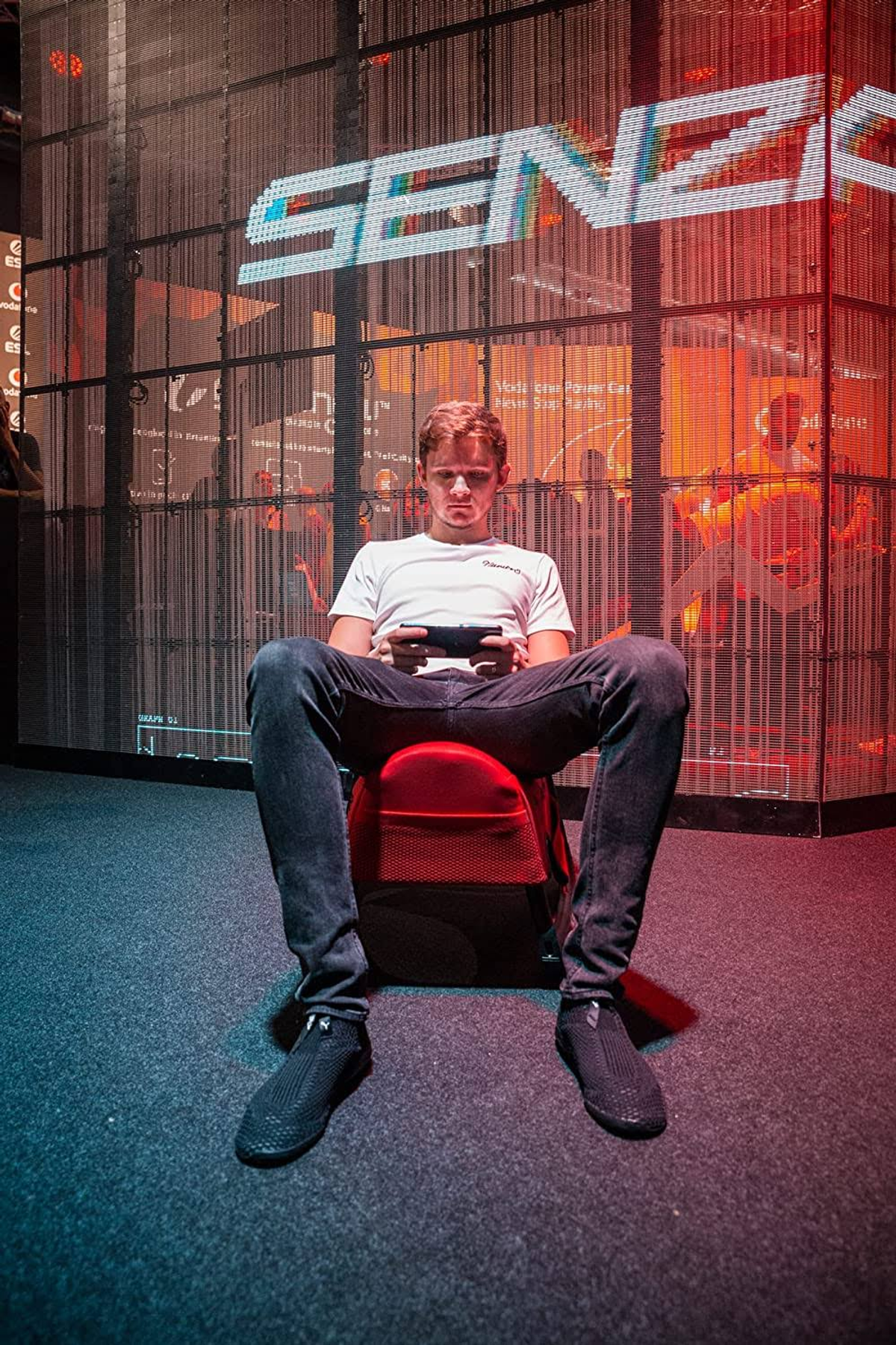 Een jonge man zit en speelt op een handheld console. De achtergrond heeft een SENZA-logo.