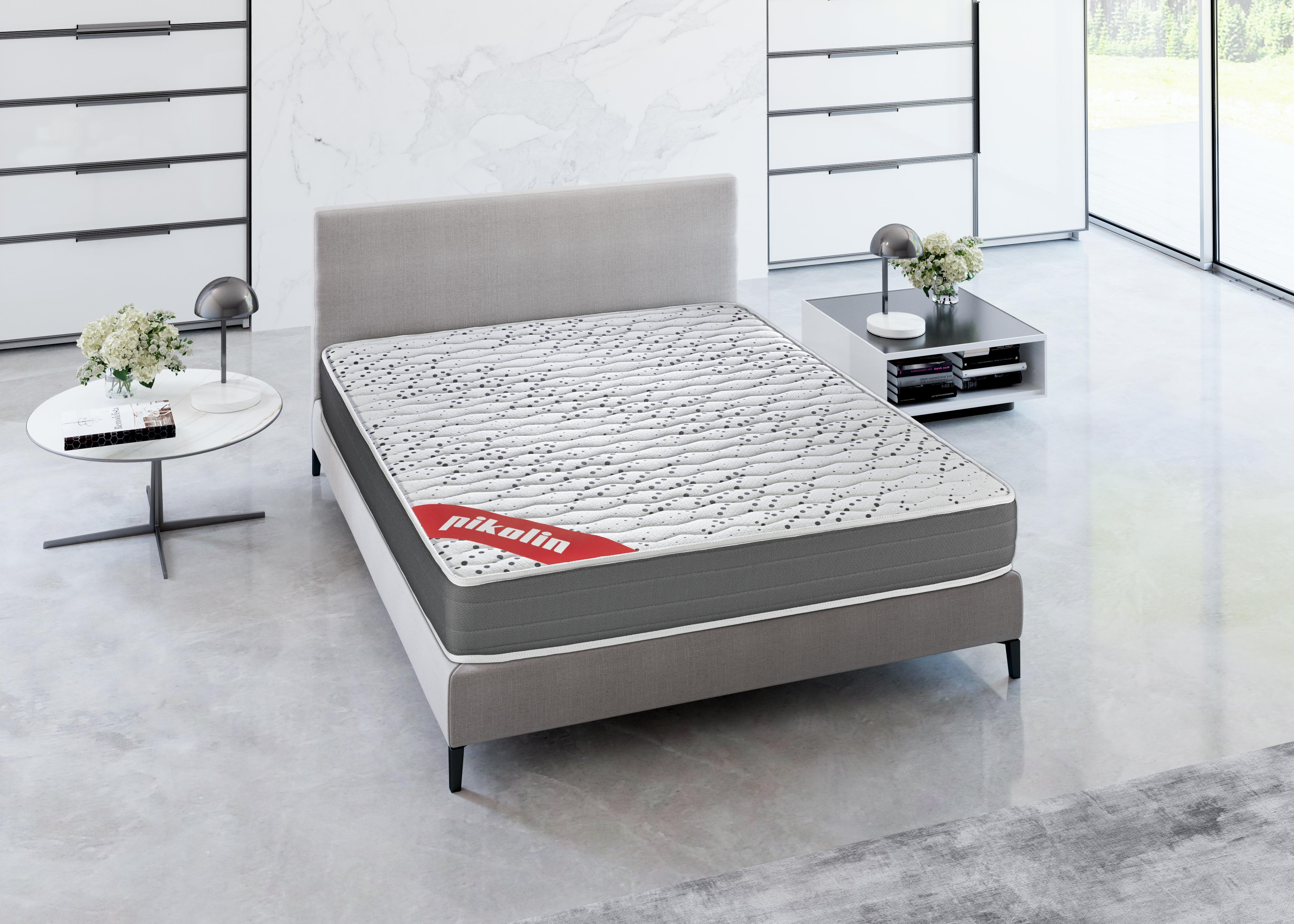 Una cama con colchón blanco y marco gris en una habitación luminosa.