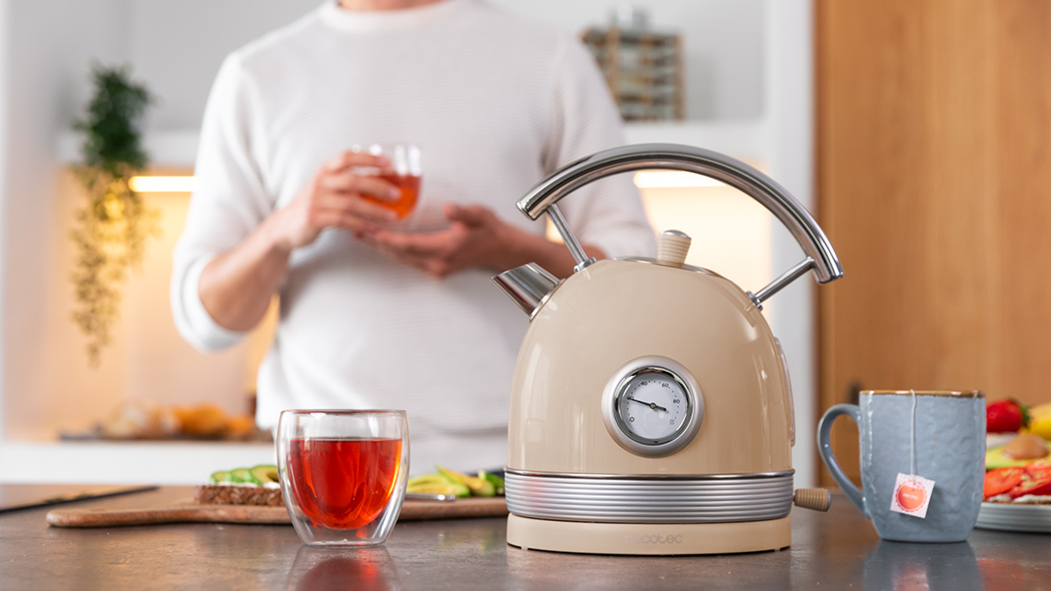 Osoba w kuchni robi herbatę. Na blacie stoi czajnik, dwie filiżanki i kanapka.