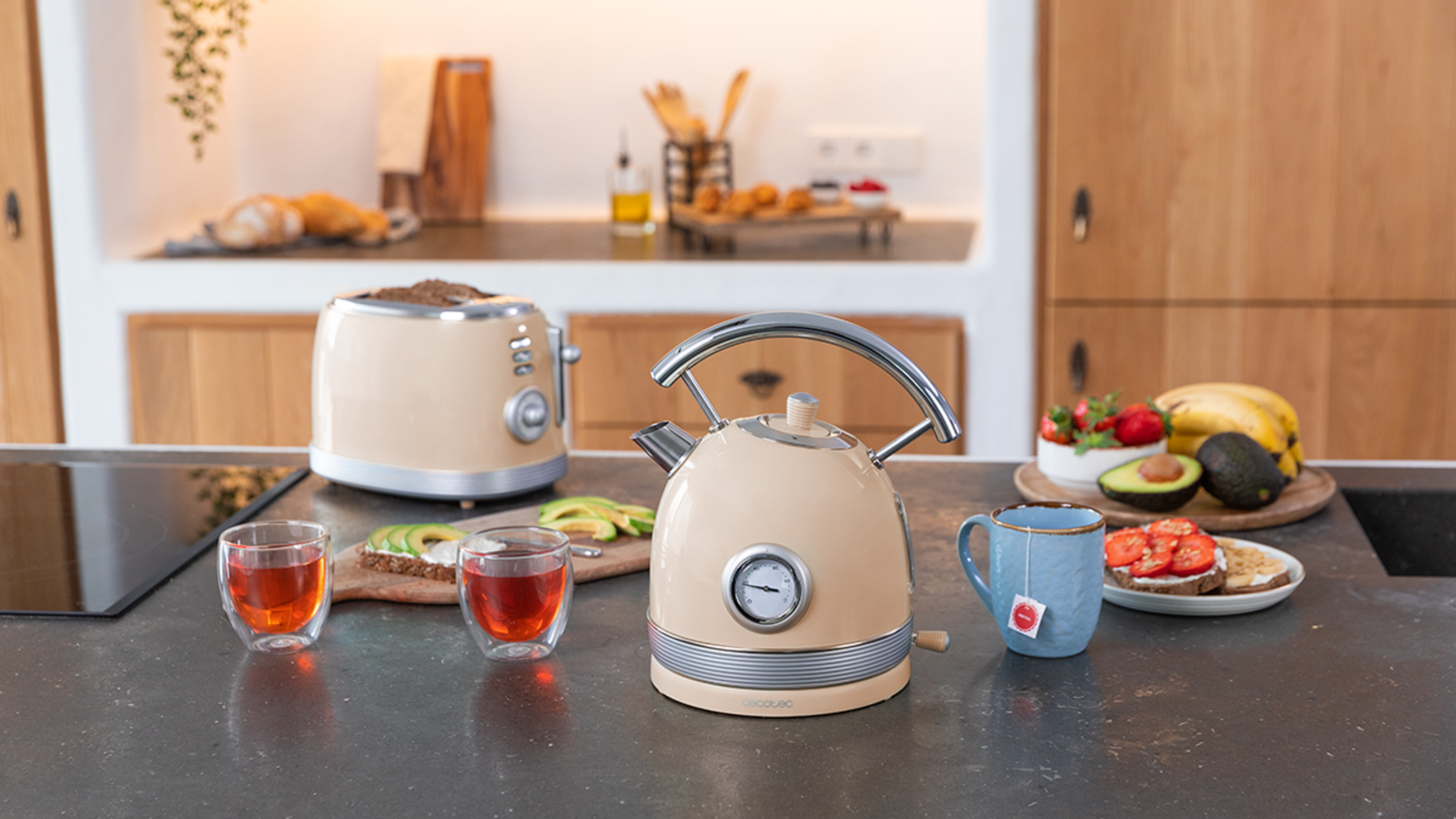 Blat kuchenny z tosterem, czajnikiem, filiżankami do herbaty, plasterkami awokado i owocami, na czarnej powierzchni.