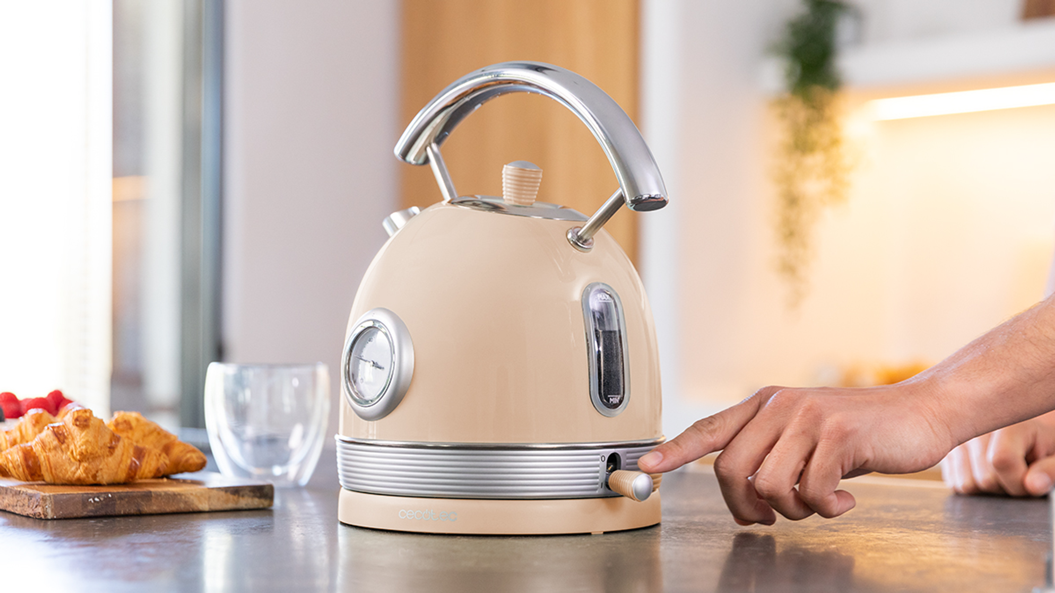 Beżowy czajnik elektryczny na blacie, ręka osoby przekręca pokrętło.