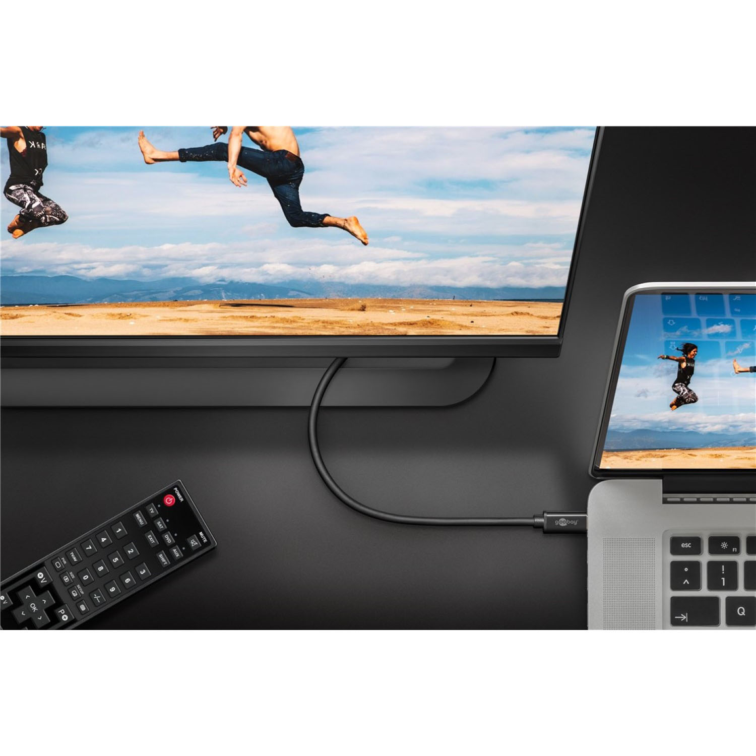 Fernsehbildschirm, Laptop und Fernbedienung. Menschen springen auf dem Fernseher, Himmelshintergrund. Schwarzer Schreibtisch.