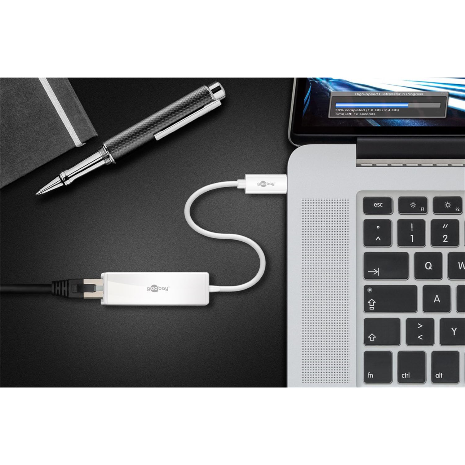 Laptop, der über ein weißes Kabel mit einem GoBay-Gerät verbunden ist. Stift und Notizbuch sichtbar.