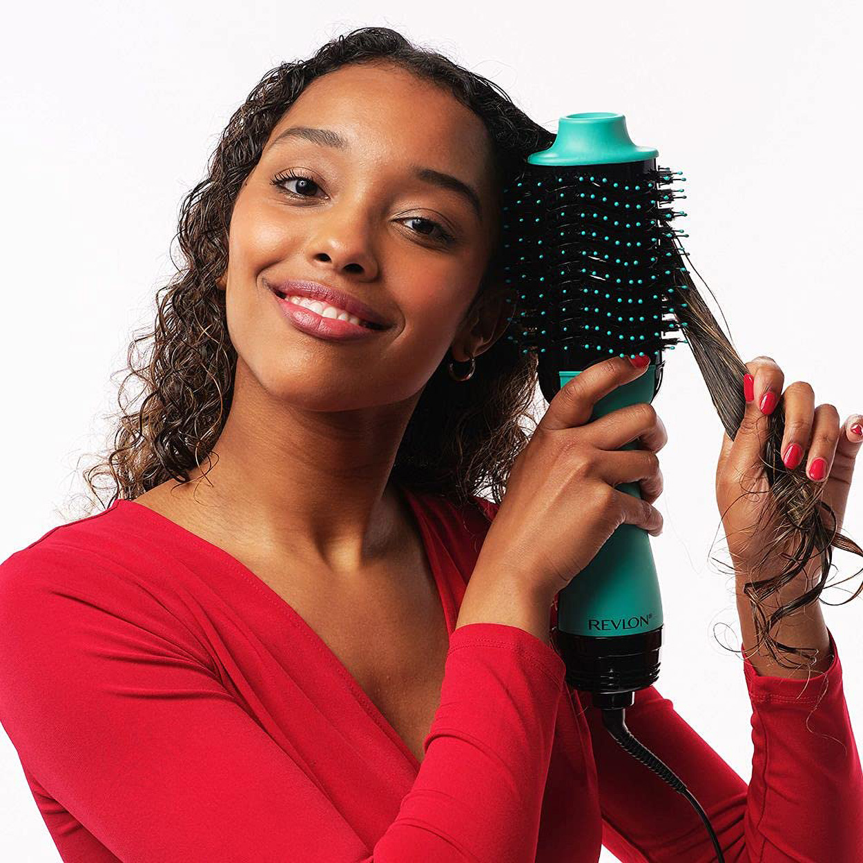 Vrouw die een turquoise föhnborstel gebruikt, lacht naar de camera. Ze heeft krullend haar en rode nagellak.