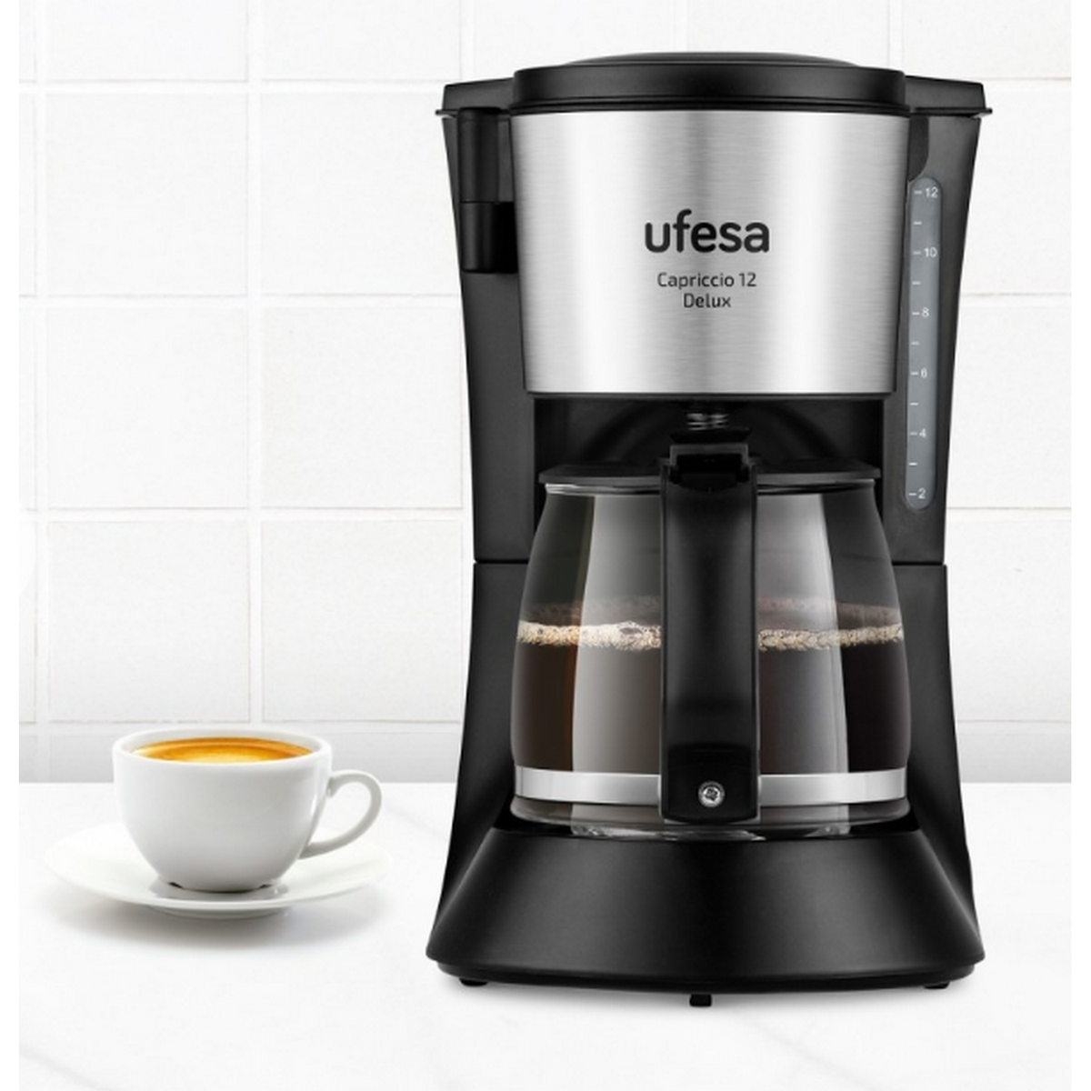 Czarno-srebrny ekspres do kawy ze szklanym dzbankiem i filiżanka kawy na białej powierzchni.