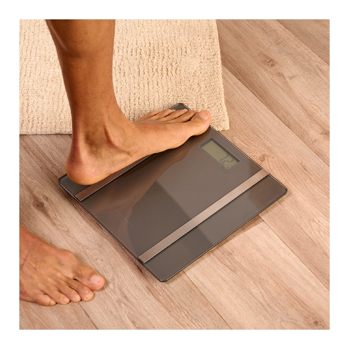 Stopa na wadze cyfrowej w łazience. Waga pokazuje 12.0, podłoga jest drewniana.