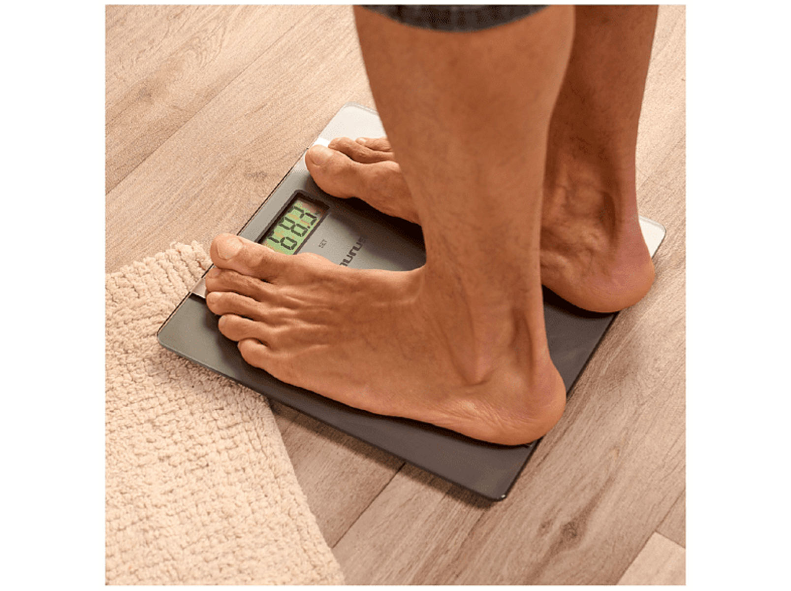 Bose stopy na wadze cyfrowej. Wyświetlacz pokazuje 68,3. Biały ręcznik leży na podłodze.