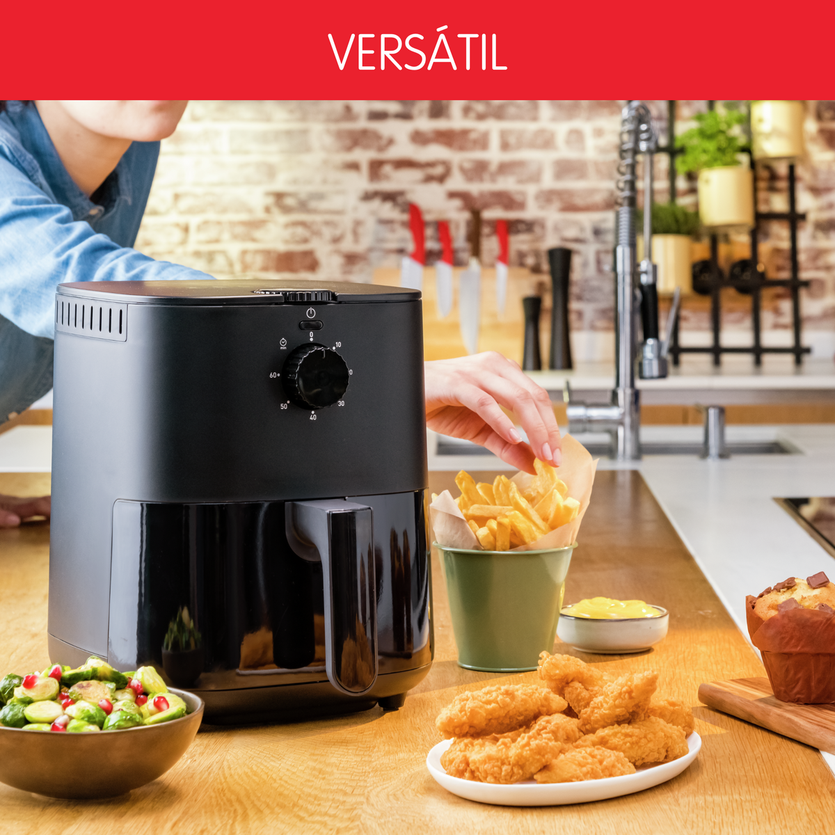 Friggitrice ad aria nera con cibo: patatine fritte, bocconcini di pollo, muffin e verdure. Banner rosso: VERSÁTIL.
