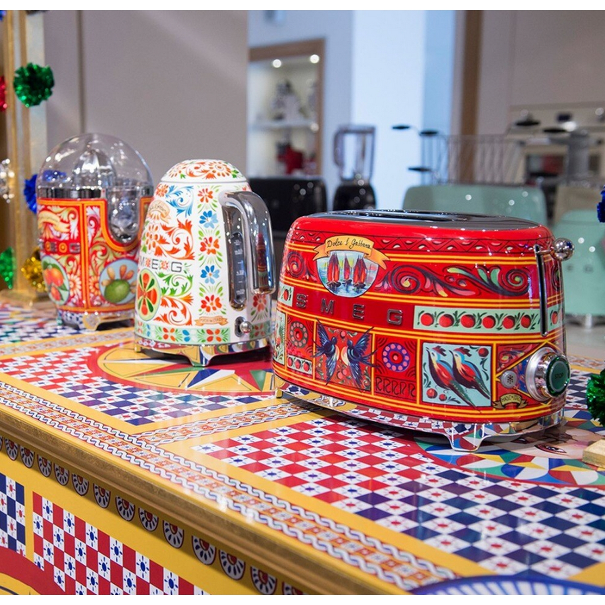 Tres tostadoras y una tetera coloridas de Dolce & Gabbana sobre una mesa decorada.