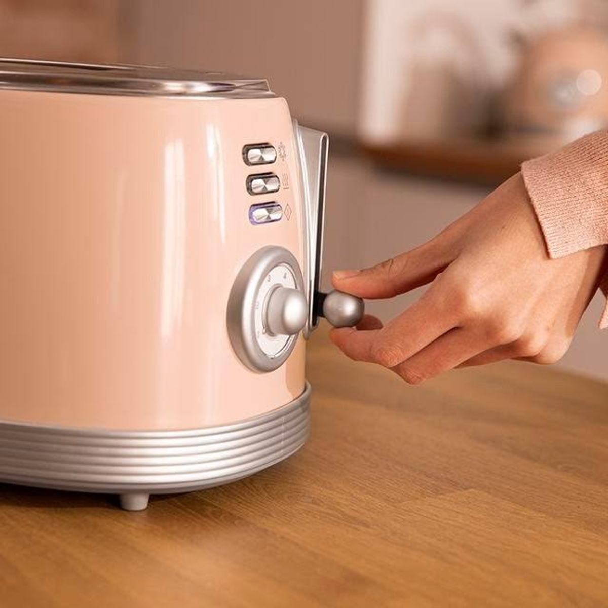 Hand einer Person, die einen rosa Toaster auf einer Holzoberfläche bedient. Verschwommener Hintergrund.