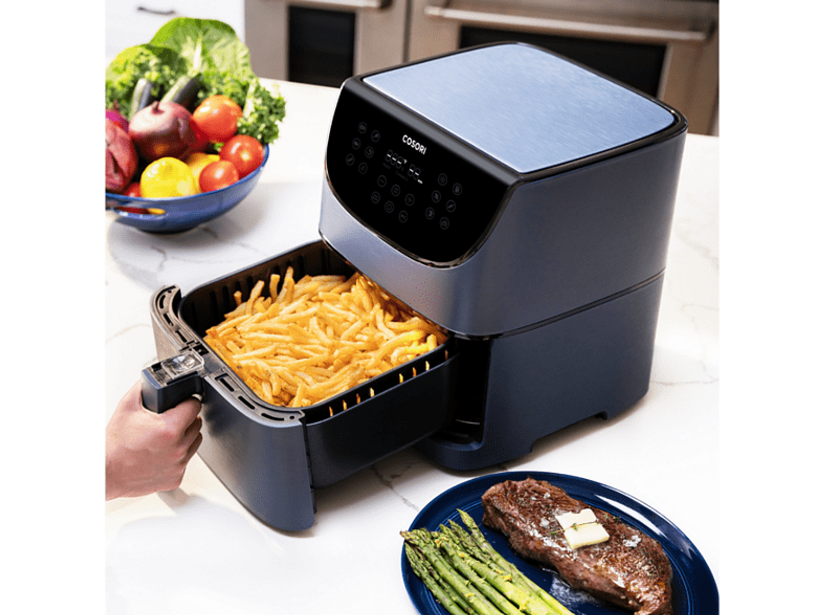 Blauer Airfryer mit Pommes, Teller mit Steak und Gemüse.