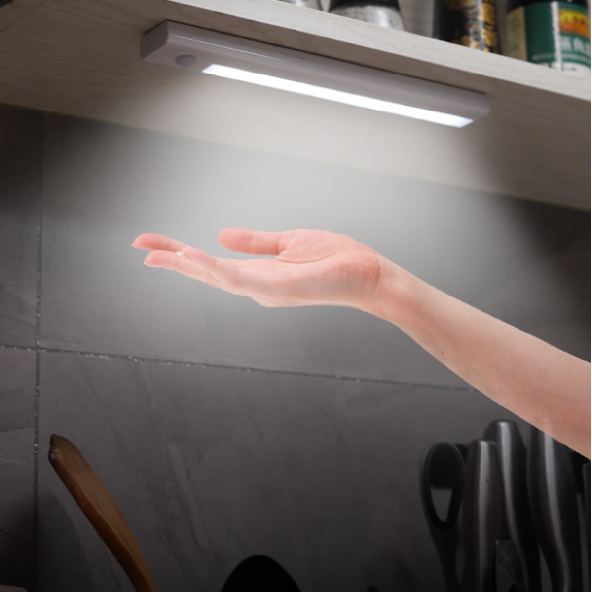 Hand reaching towards a lit LED light strip under a shelf in a kitchen.