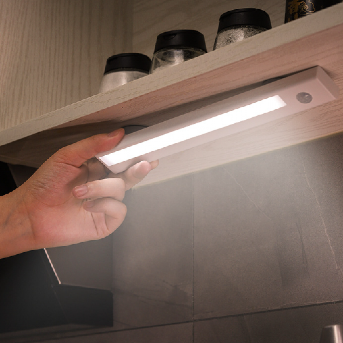 Hand turning on an LED light bar mounted under a cabinet.