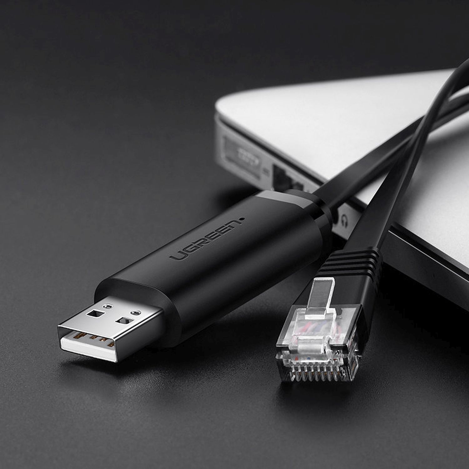 Schwarzes USB-zu-Ethernet-Kabel, an einen Laptop angeschlossen, auf dunkler Oberfläche.