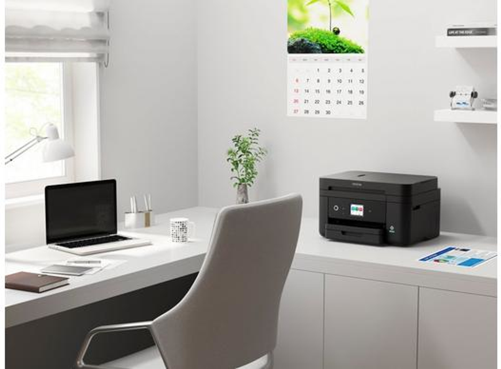 Un bureau à domicile bien éclairé avec un ordinateur portable, une imprimante et un calendrier sur un bureau blanc.