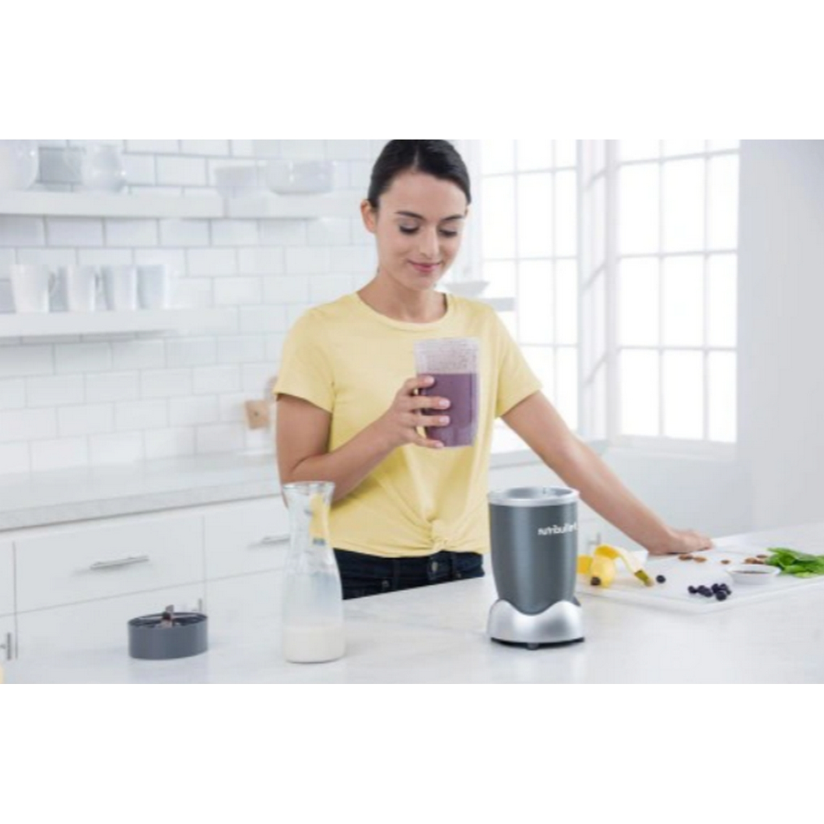Una mujer hace un batido en una licuadora. Sostiene el vaso con el batido.