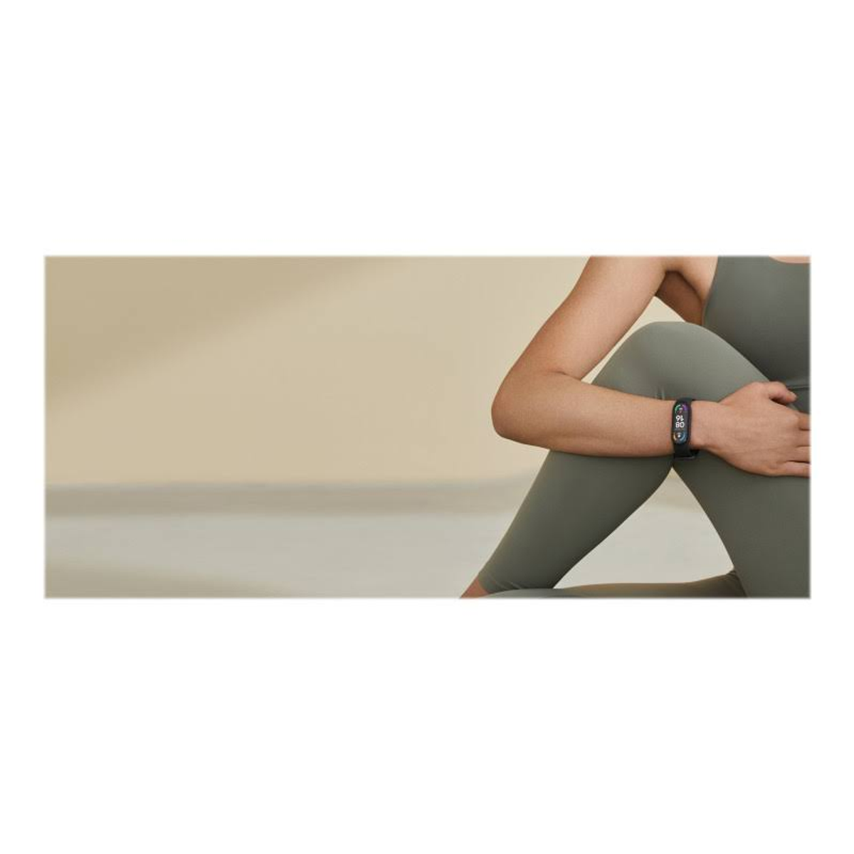 Frau mit Fitnesstracker, sitzend. Olivgrünes Outfit, neutraler Hintergrund.