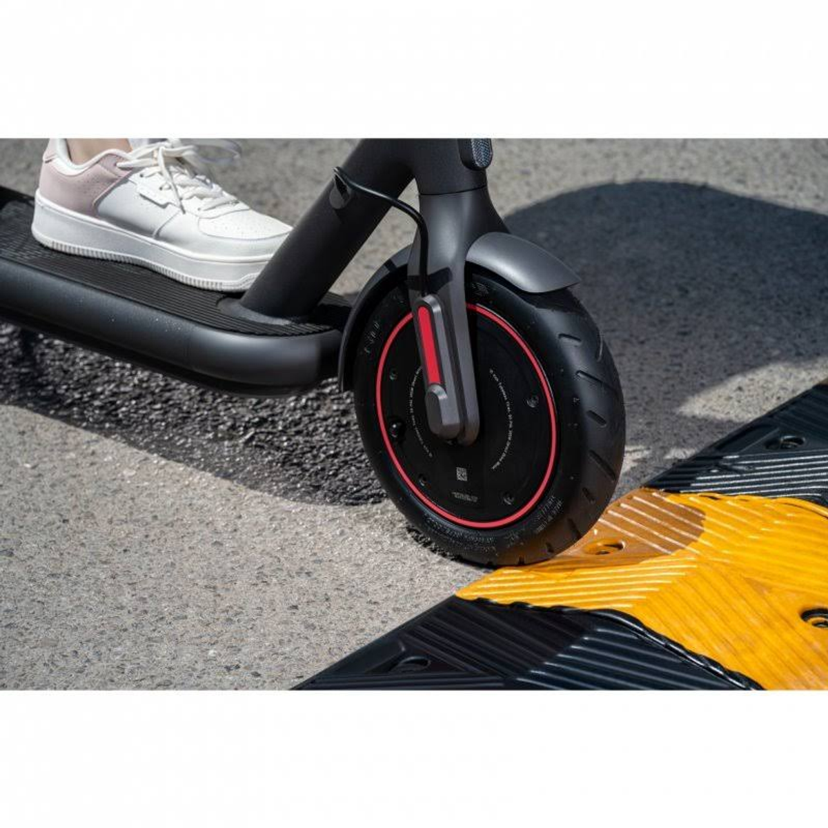 Persona en patinete eléctrico negro y rojo, con badén amarillo, en asfalto.