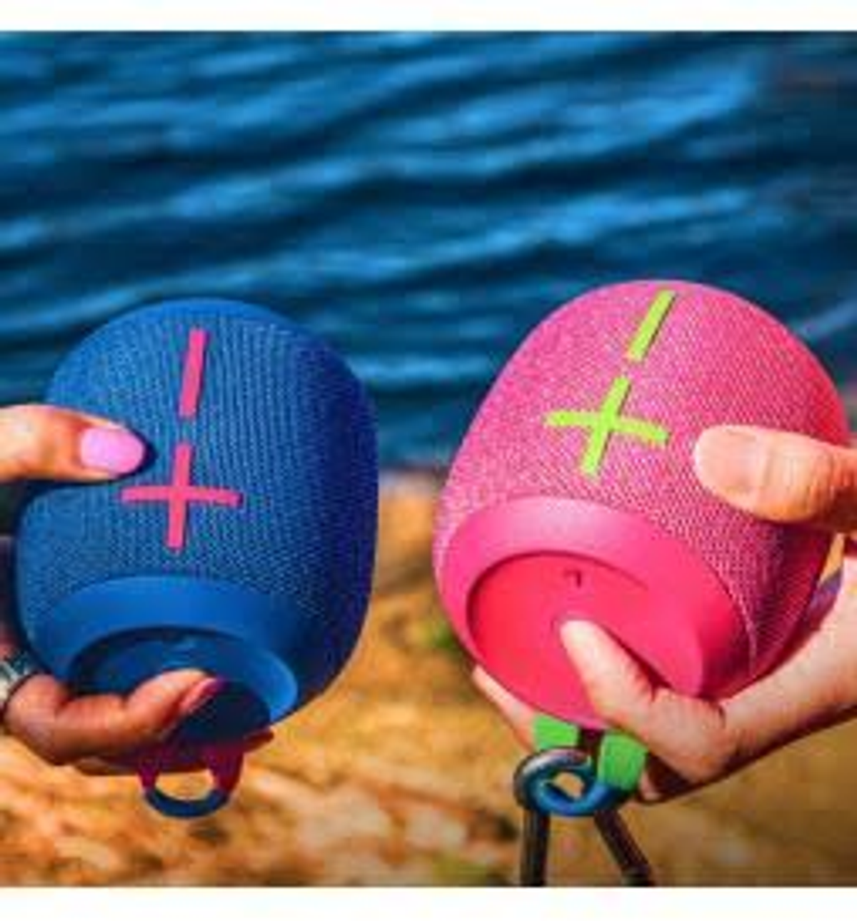 Dwa głośniki, jeden niebieski i jeden różowy, trzymane w dłoniach. Głośniki mają krzyżowy wzór.