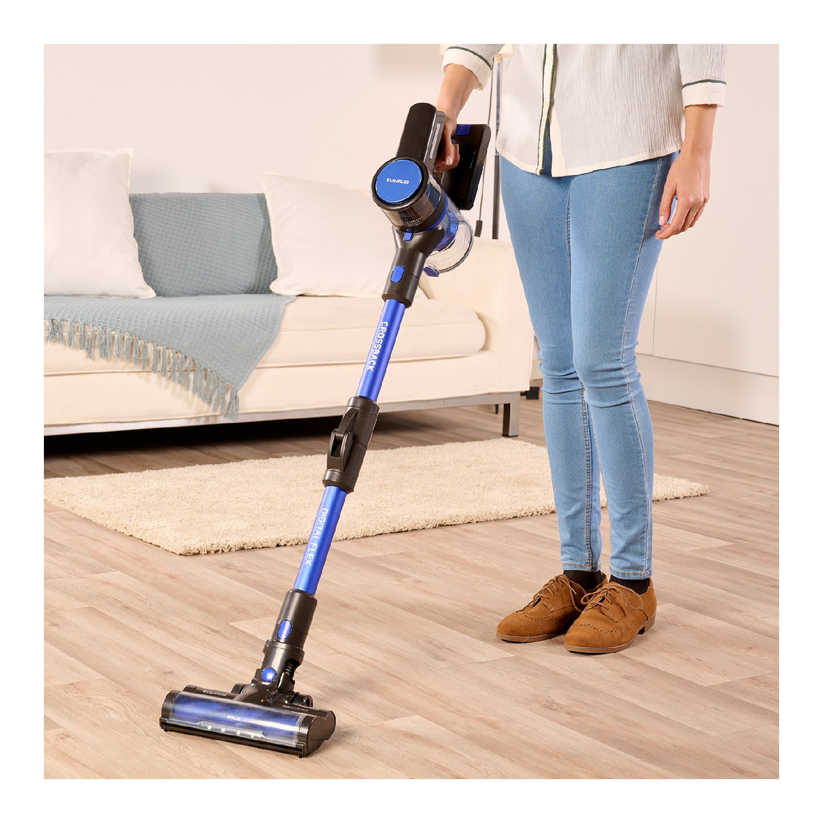 Mujer aspirando una habitación. La aspiradora es azul y negra. Suelo de madera clara.