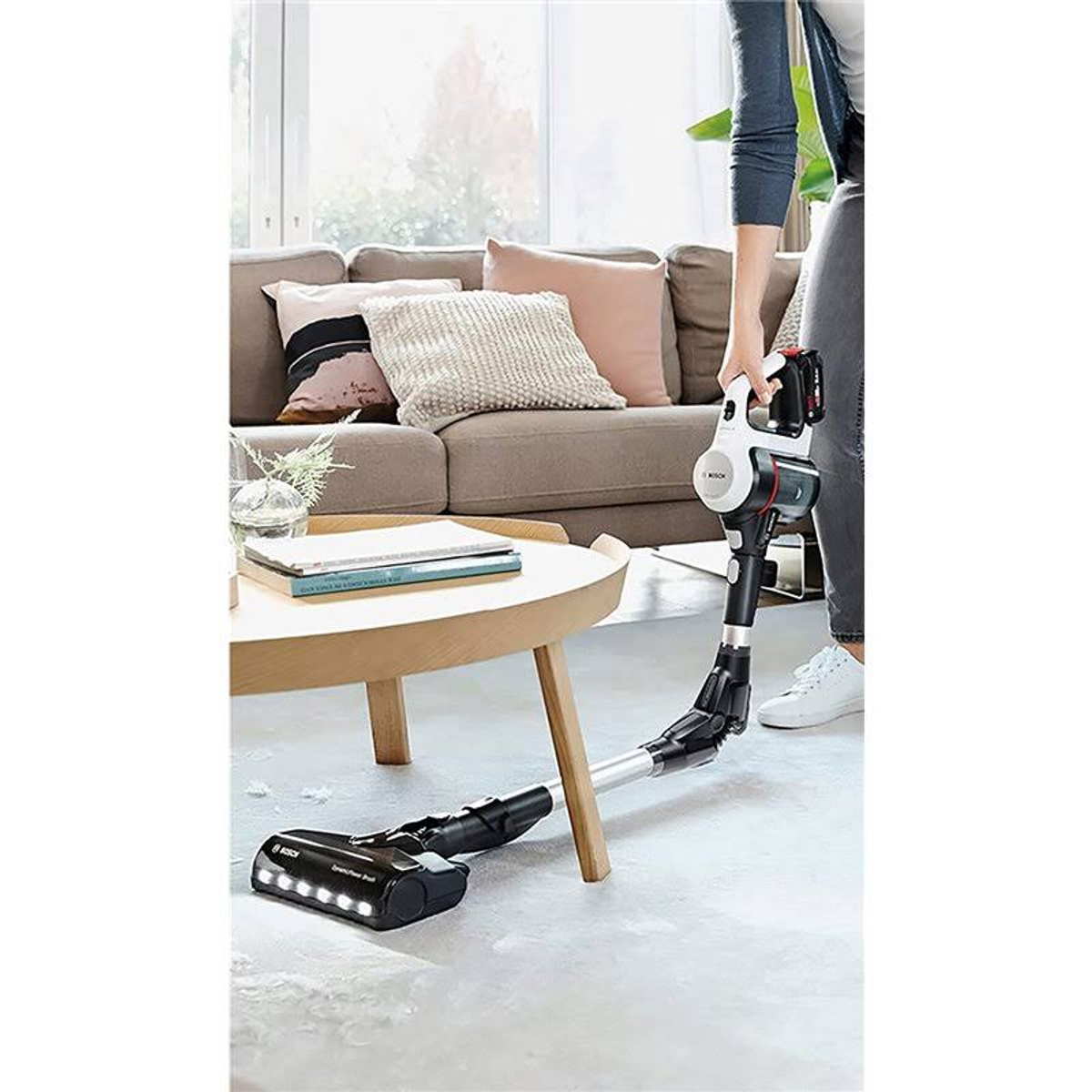 Une personne passant l'aspirateur dans un salon avec un aspirateur blanc et noir. Un canapé est en arrière-plan.