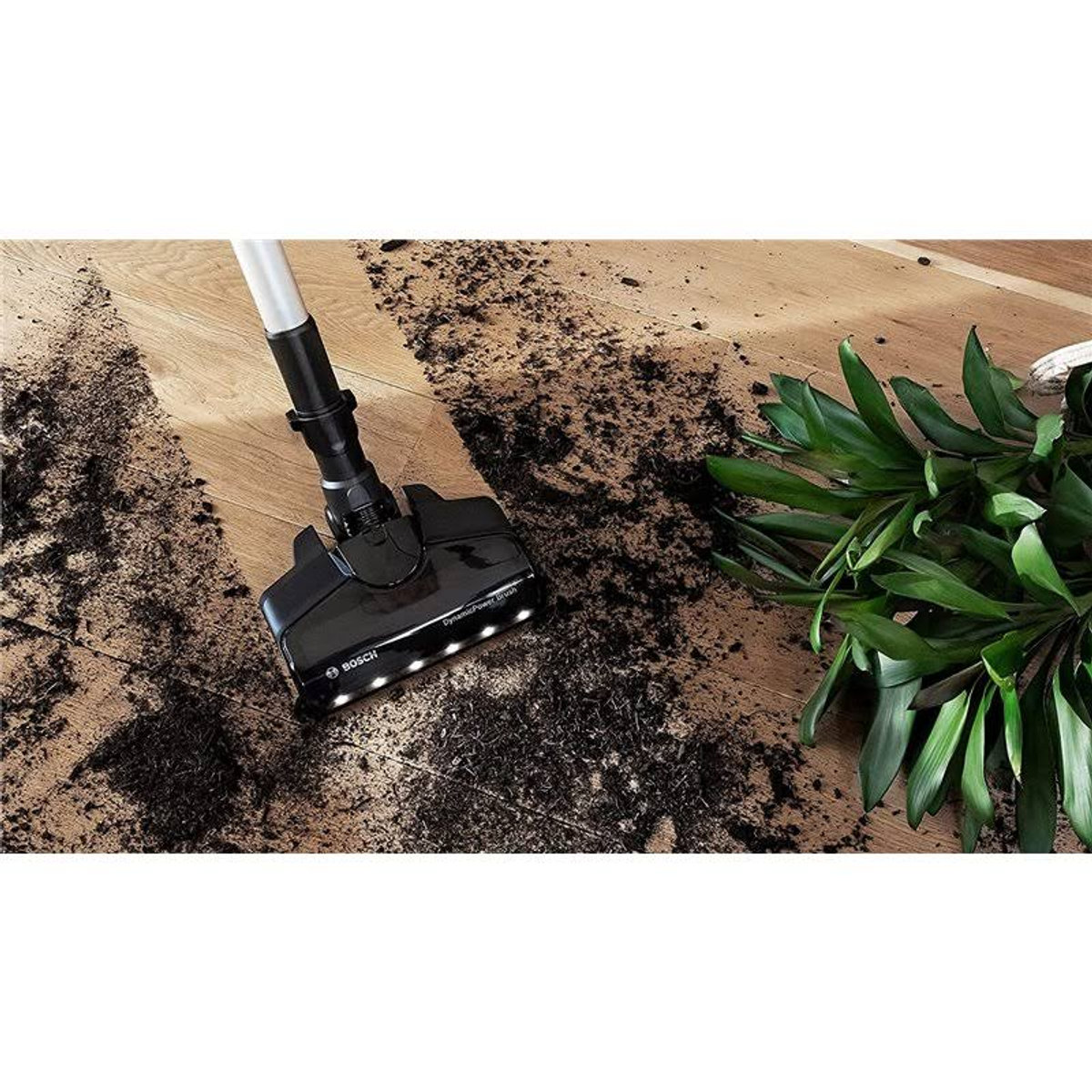 Tête d'aspirateur nettoyant un sol en bois avec saleté et débris végétaux.