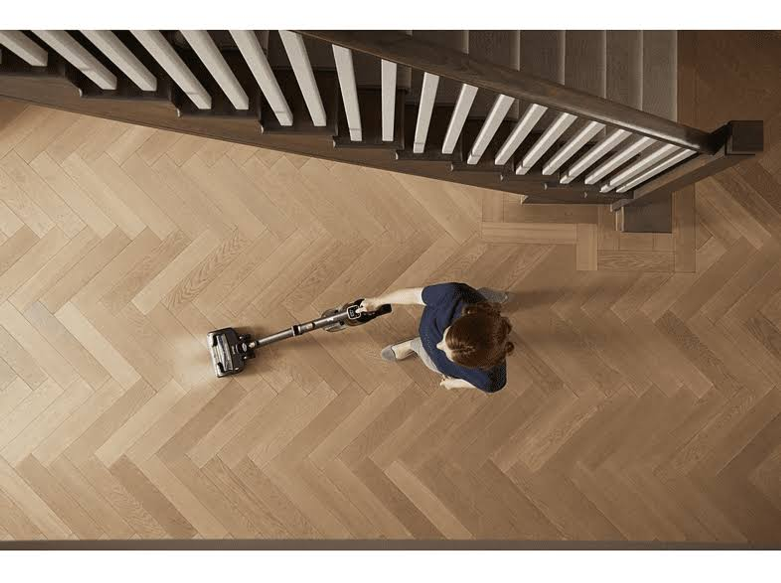 Draufsicht einer Person, die einen Holzboden in der Nähe einer Treppe saugt.