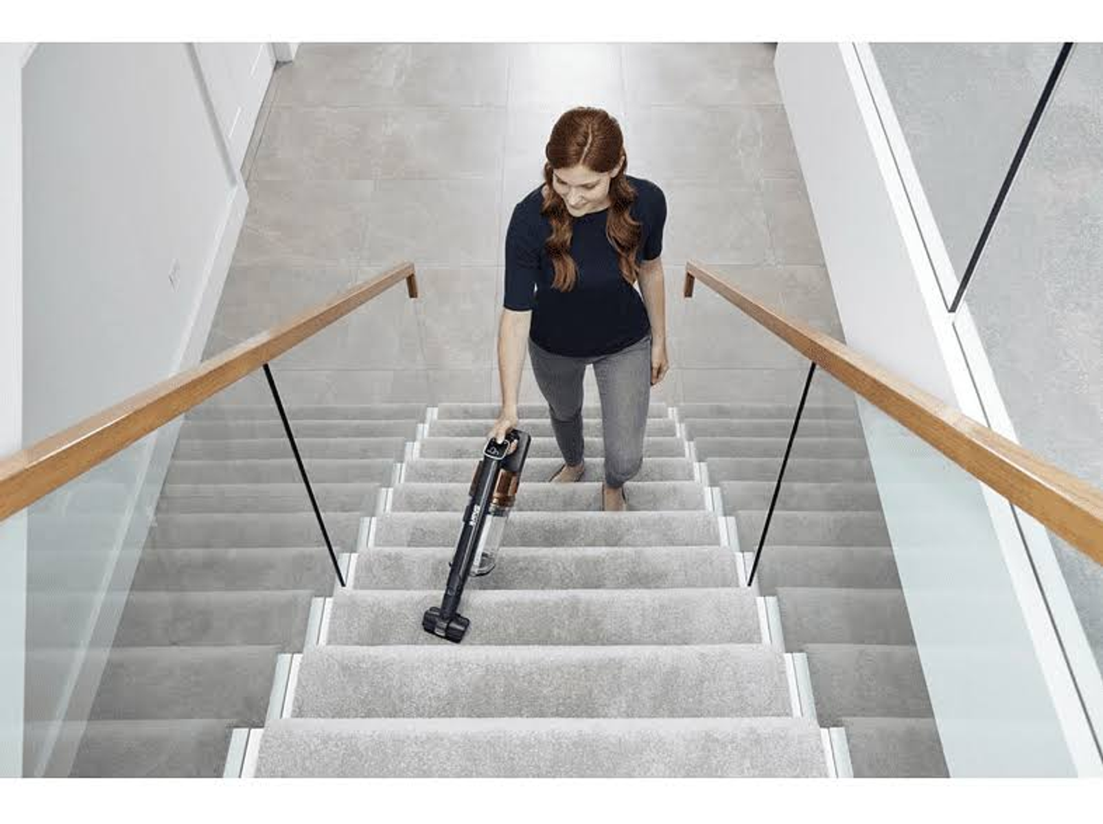 Frau, die Treppen saugt. Eine Frau, die Teppichtreppen mit einem kabellosen Staubsauger saugt.