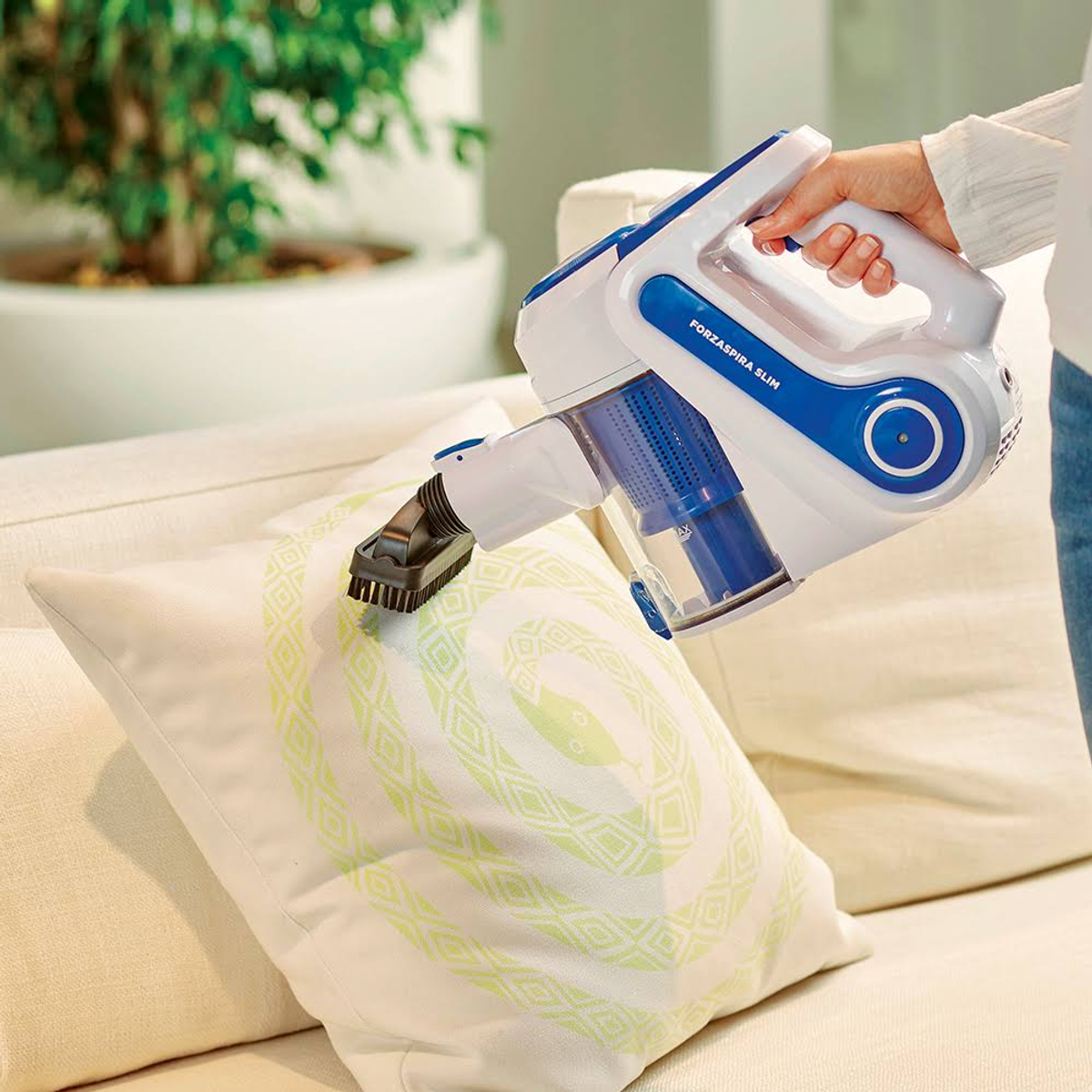 Un aspirapolvere portatile bianco e blu viene utilizzato per pulire un cuscino.
