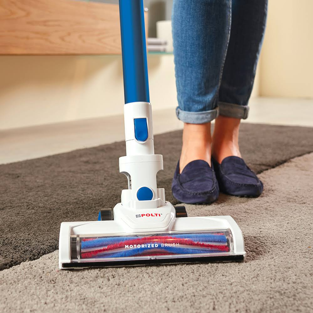 Aspirapolvere su un tappeto, con manico blu e bianco e gambe di donna.