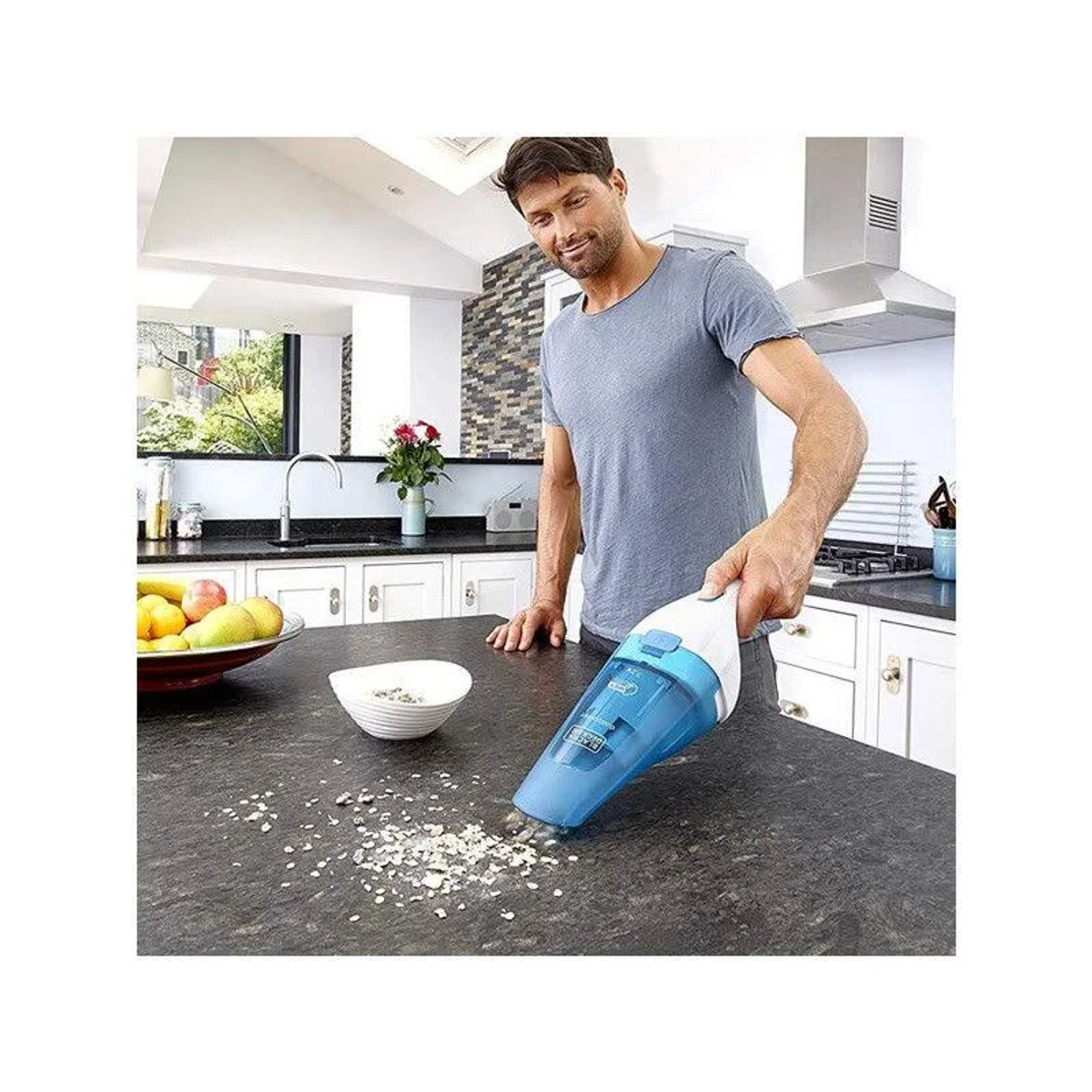 Hombre limpiando encimera con aspiradora de mano azul y blanca. Escena de cocina.