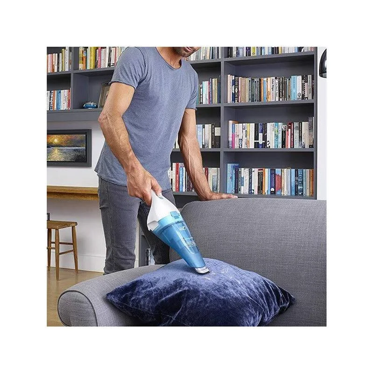 Hombre aspira una almohada de terciopelo azul en un sofá con estantería.