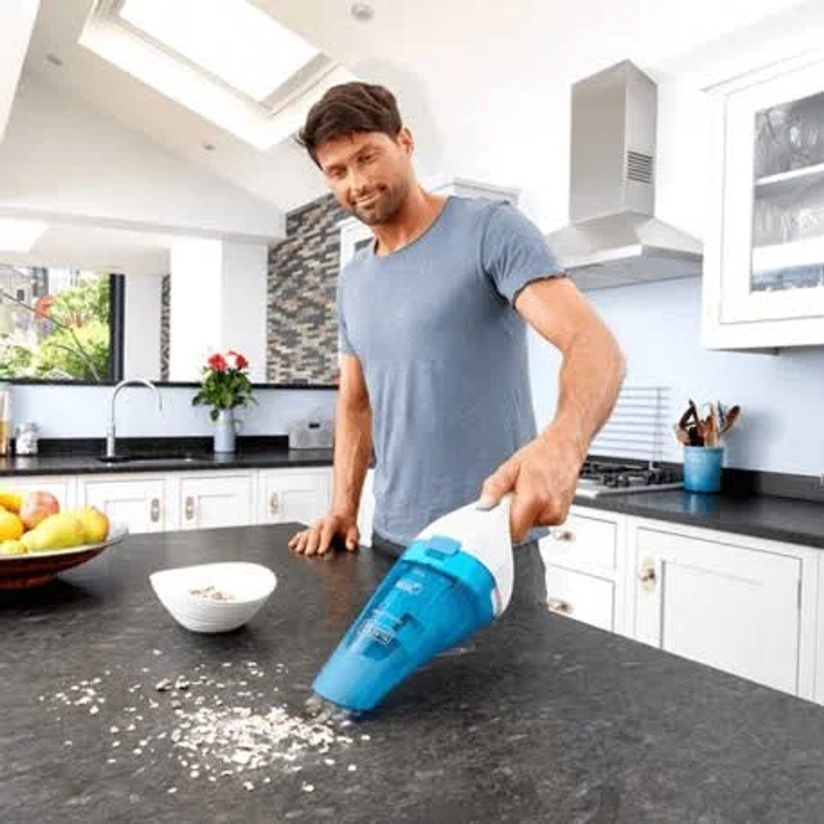 Un hombre usando una aspiradora de mano en una encimera de cocina con migas.