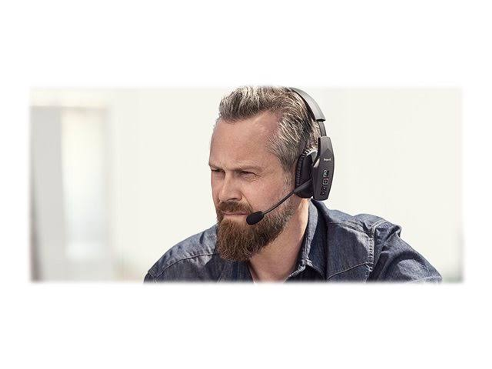 Mężczyzna z brodą w czarnych słuchawkach z mikrofonem, patrzący w bok.
