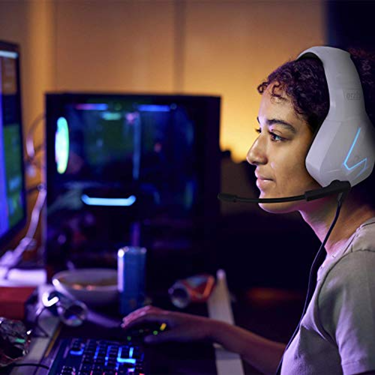Donna con cuffie da gioco bianche, che guarda un monitor. Tastiera e mouse visibili.