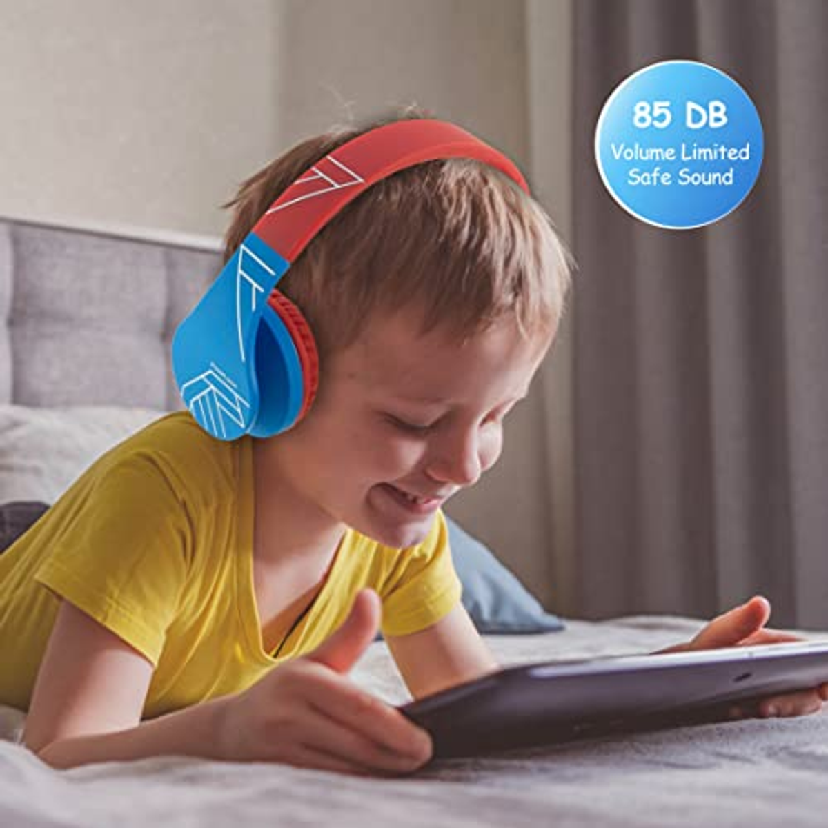 Un ragazzo con cuffie colorate, guarda un tablet. Le cuffie sono blu e rosse.