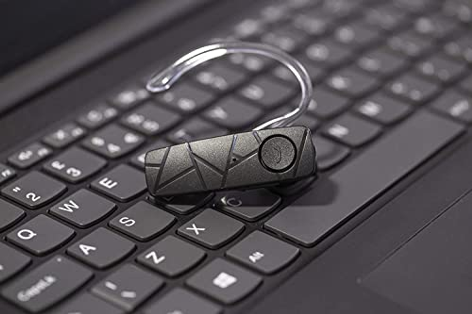 Schwarzes Bluetooth-Headset auf einer Laptop-Tastatur. Hat ein gebogenes Design und einen Knopf.