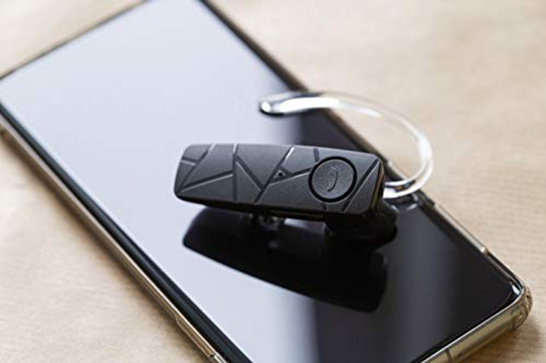 Schwarzes Bluetooth-Headset an einem Smartphone befestigt. Das Headset hat einen Knopf und einen gebogenen Haken.