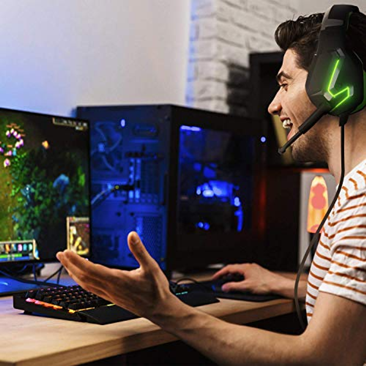 Uomo con cuffie da gioco. Due monitor, tastiera, PC gaming e lampada colorata.