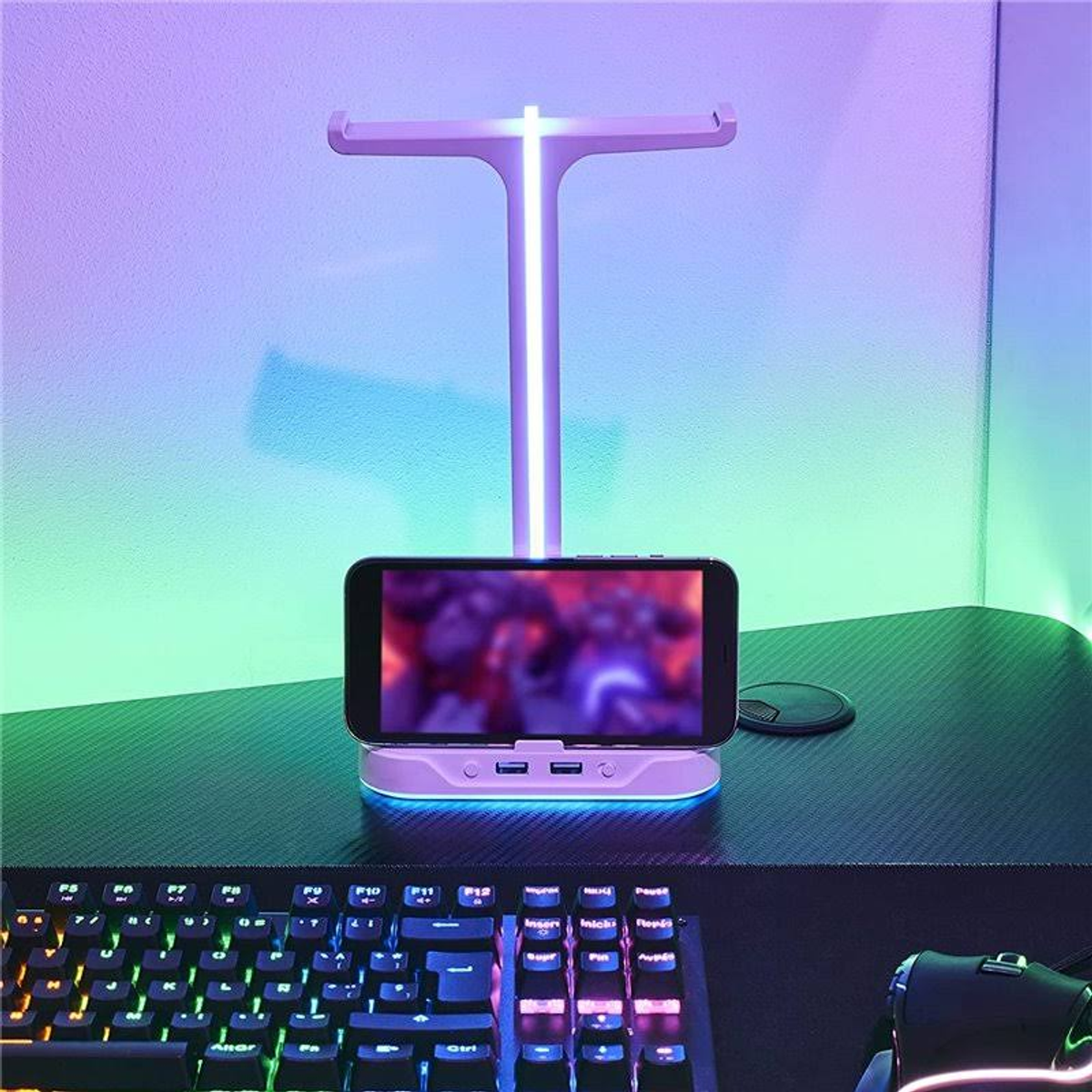 Un teléfono en un soporte con teclado y ratón en primer plano, todo iluminado con iluminación RGB.