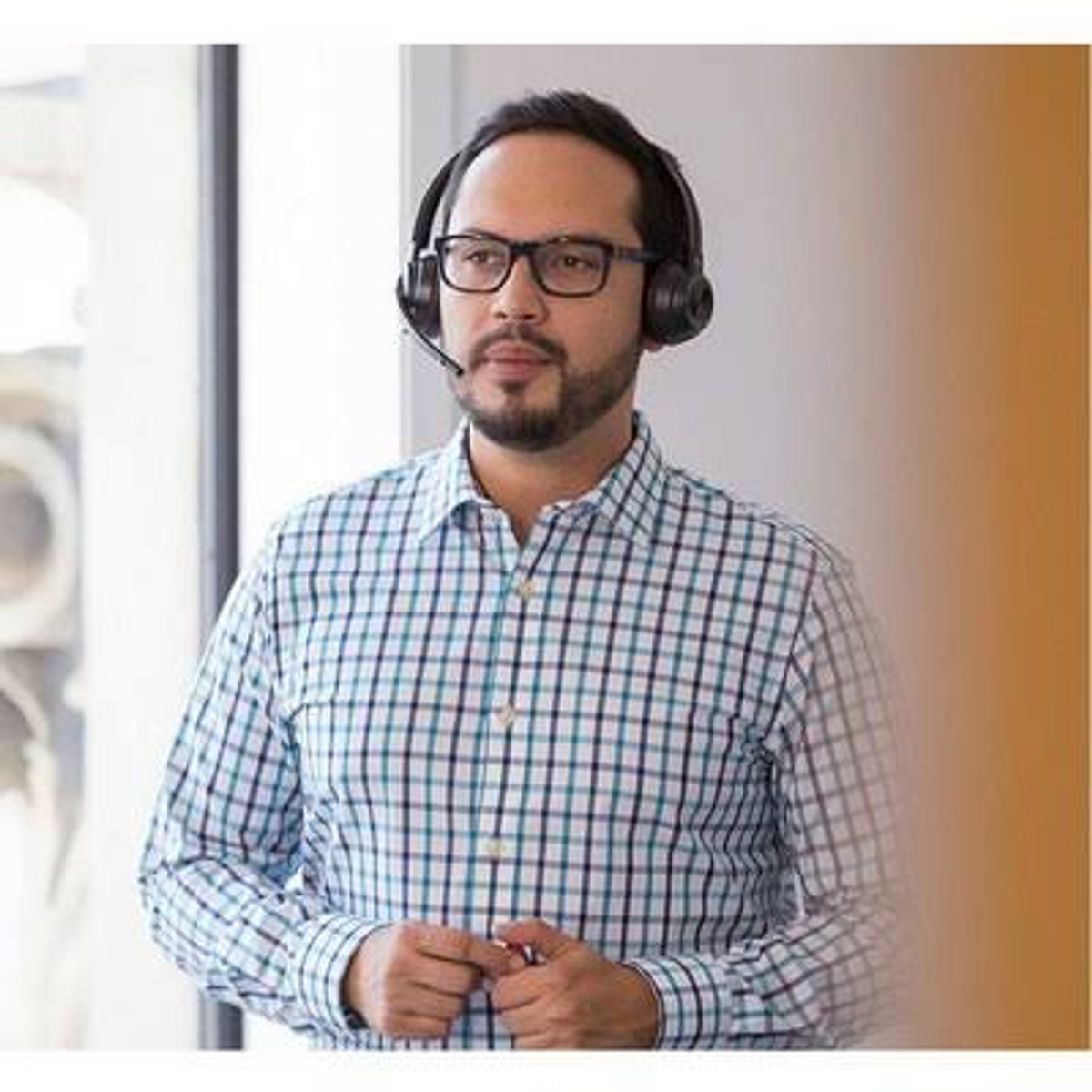 Un homme portant des lunettes et un casque avec microphone. Il porte une chemise à carreaux.