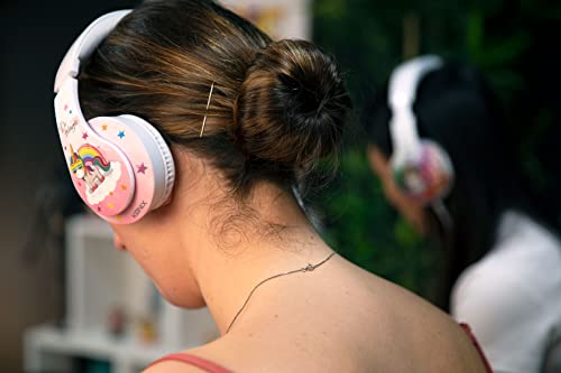 Una donna con le cuffie. Ha uno chignon. Un'altra persona indossa le cuffie sullo sfondo.